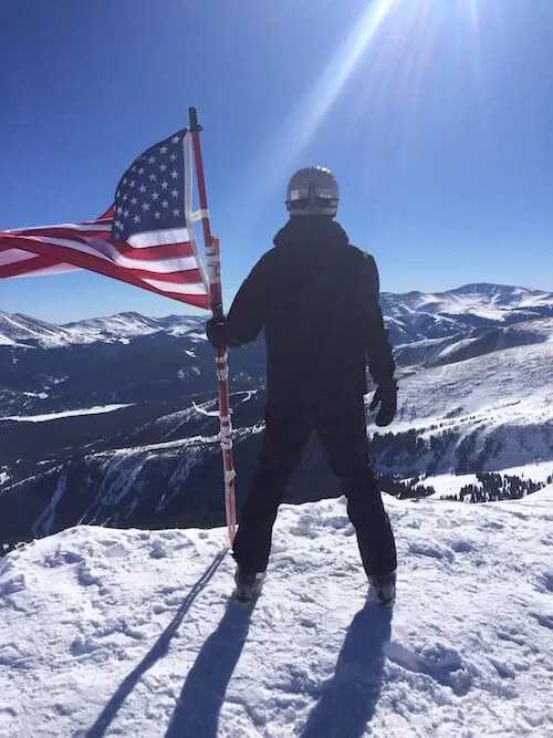 USA flag with me next to it at the top of a mountain in Breckenridge, CO